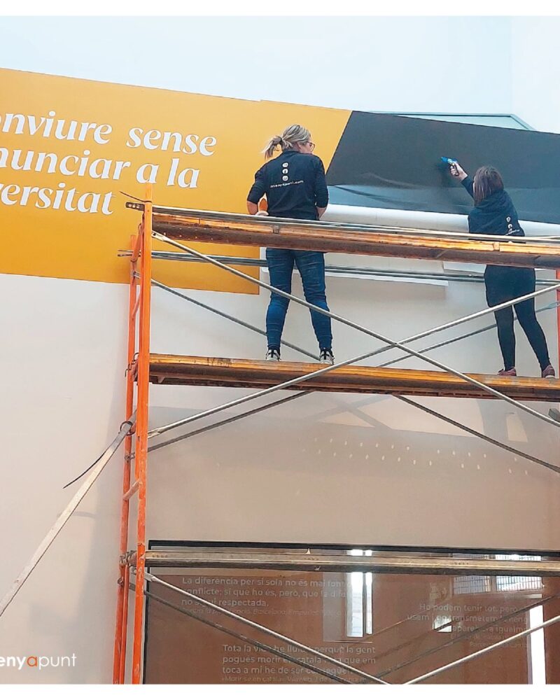 Dues persones instal·lant des d'una bastida el panell imprès d'una exposició